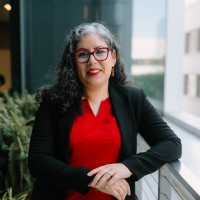 A woman with glasses in a red blouse and black blazer poses for a photo
